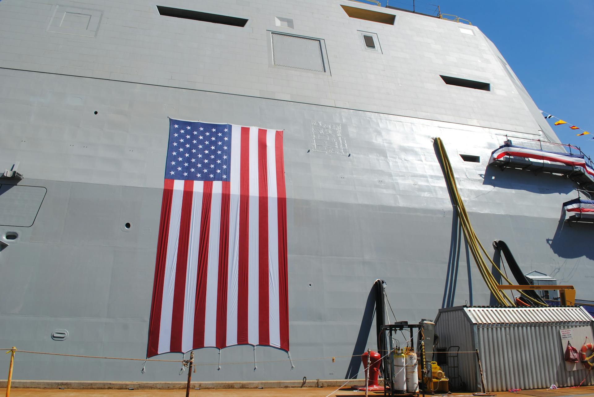 An American flag hangs on the side of a naval ship, symbolizing patriotism and maritime strength.