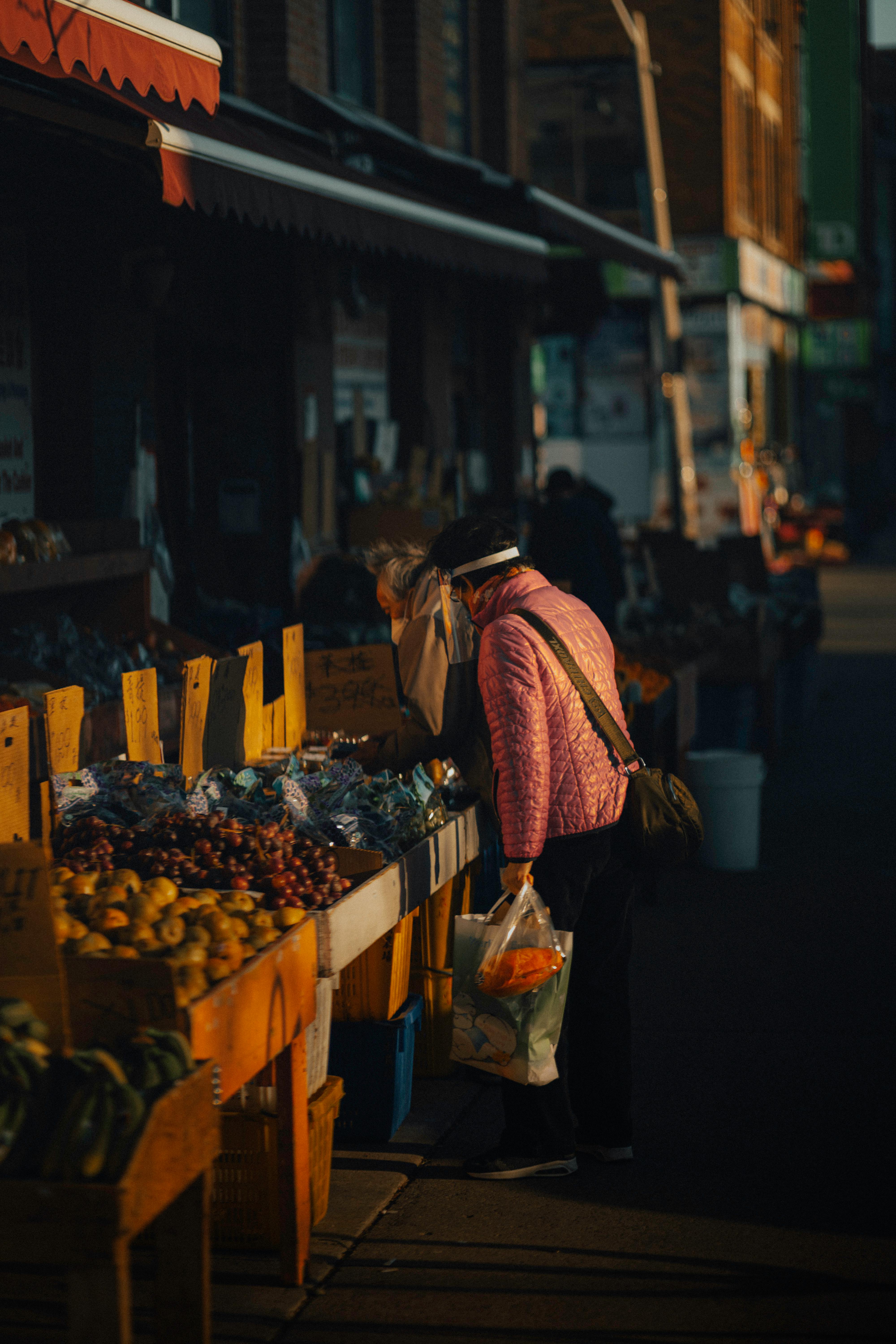 Two people shopping at a vibrant outdoor market in Toronto with fruits and warm evening light.