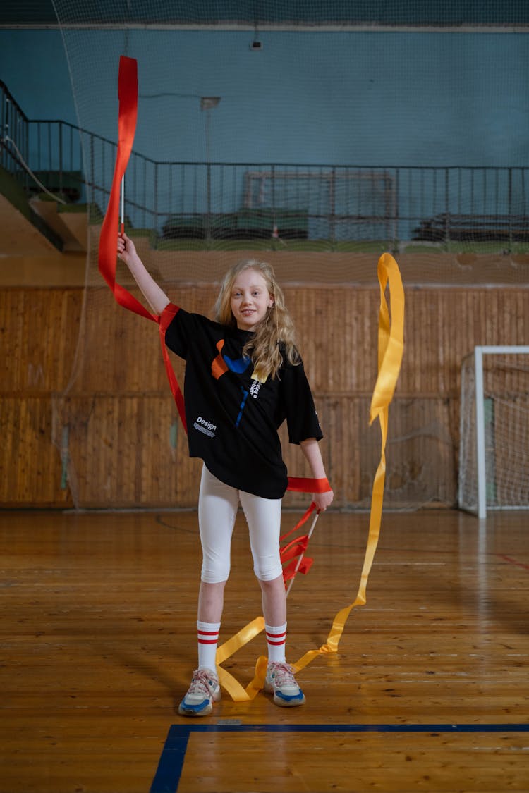 A Blonde Girl Holding Sticks With Red And Yellow Ribbons 