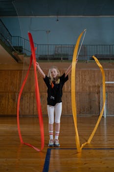 A girl practicing rhythmic gymnastics with colorful ribbons in an indoor sports hall.