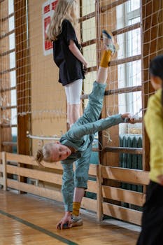 Children practicing flexibility exercises using stall bars in a gym setting.