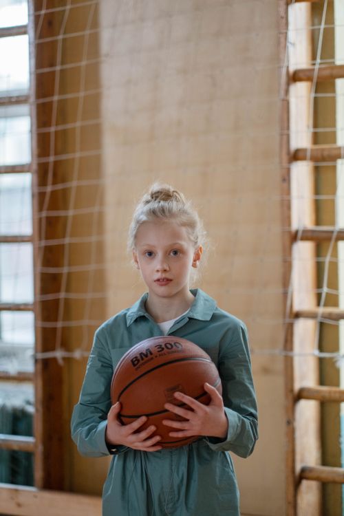 Free Caucasian girl holding basketball in indoor gym with netting in background. Stock Photo