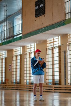 Male sports coach standing in gym, taking notes, wearing casual sportswear.