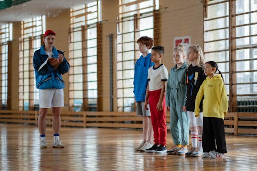 A coach instructing a diverse group of children during a gym class in a school sports hall.
