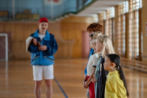Free Diverse group of children standing indoors in a gym with a coach in focus. Stock Photo