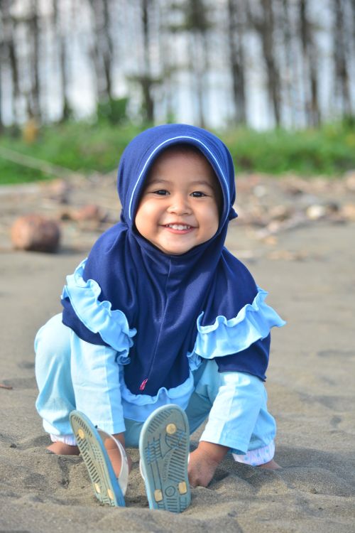 Free Charming child in blue hijab enjoying playtime on a sandy beach in Central Java. Stock Photo