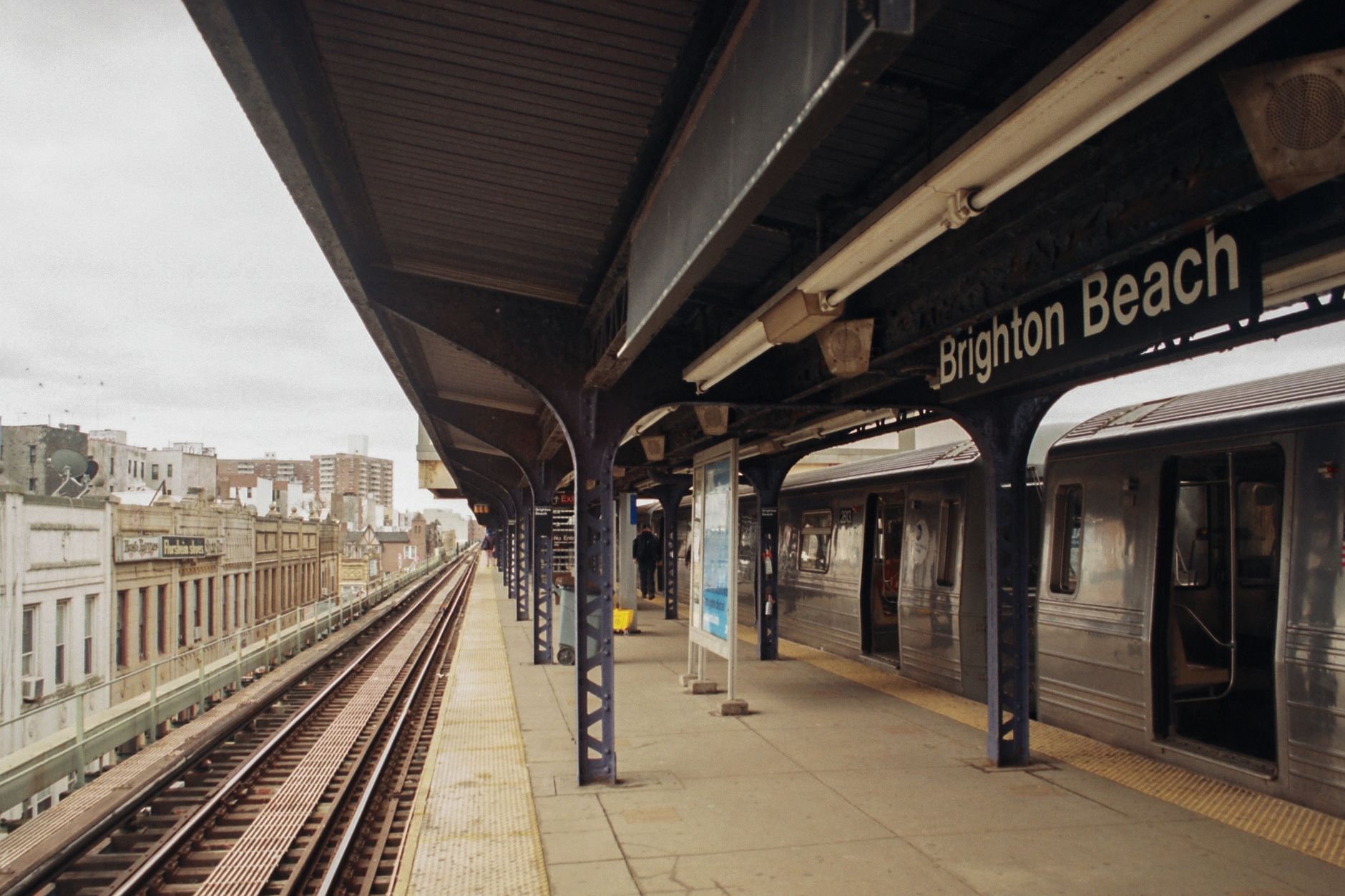 View of Brighton Beach train station platform with train and cityscape in the background.