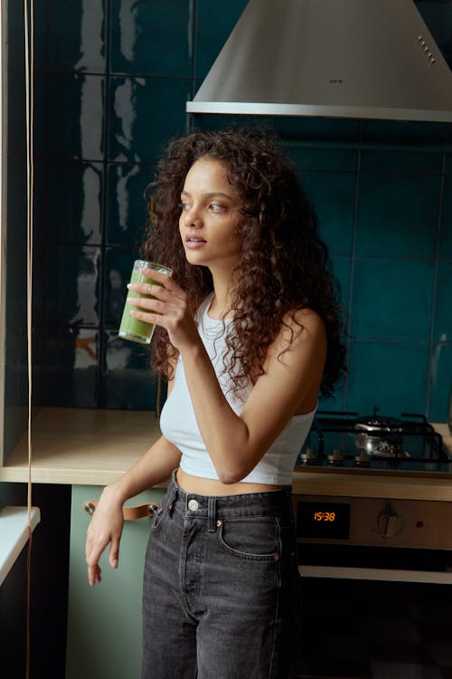 Woman in White Tank Top and Blue Denim Shorts Holding Green and Yellow Cup
