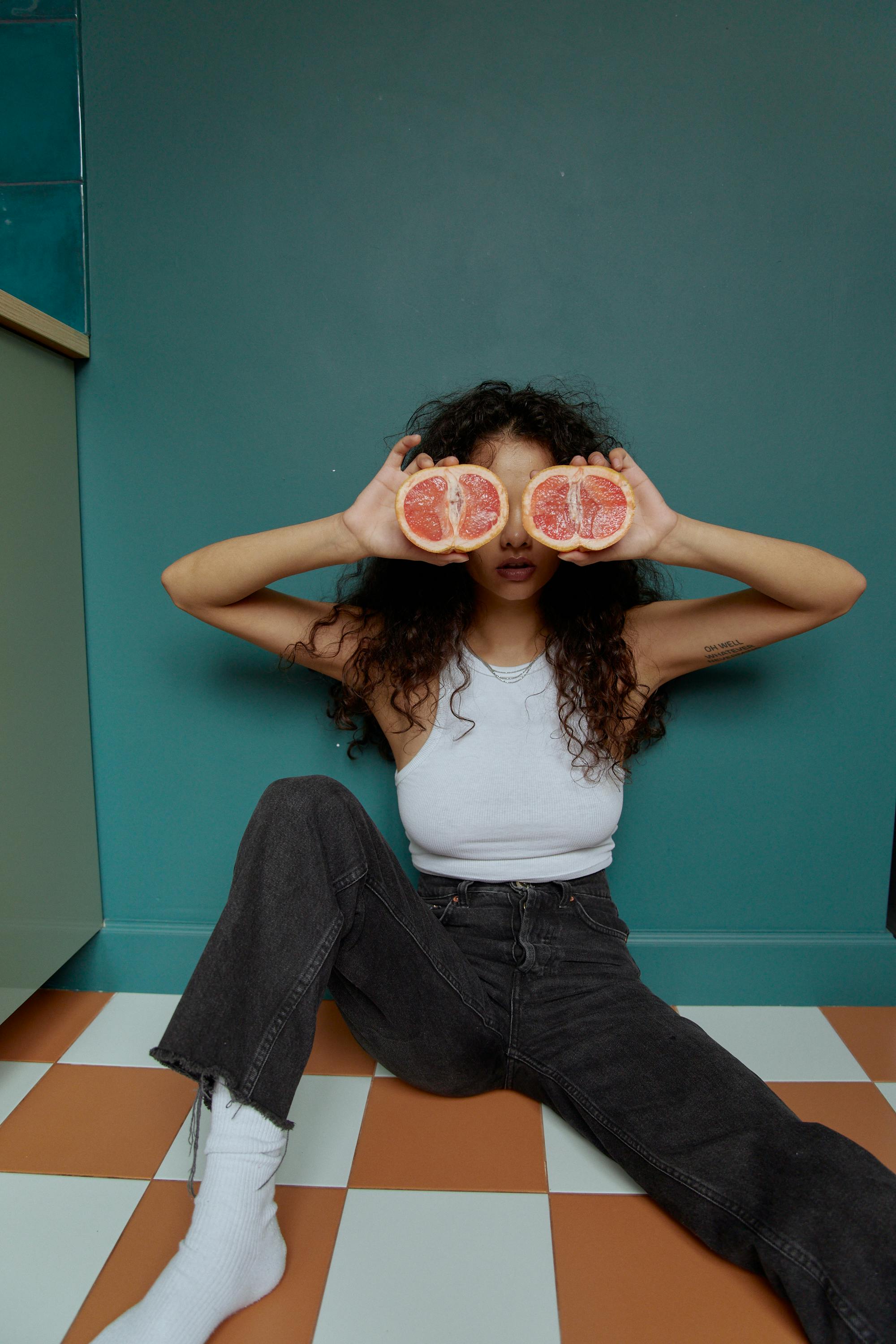 Woman in White Tank Top and Blue Denim Jeans Sitting on Blue Concrete Wall