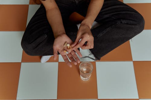 Person in Black Jeans Holding Vitamin Tablets 