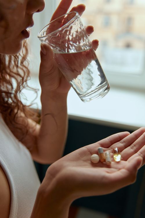 Free Close-up of a woman holding pills and a glass of water indoors. Stock Photo