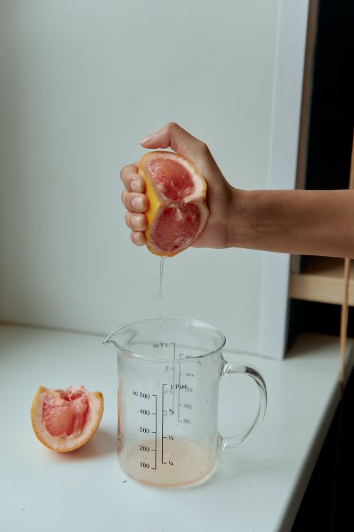 Free Close-up of a hand squeezing grapefruit juice into a measuring cup, capturing freshness and health. Stock Photo