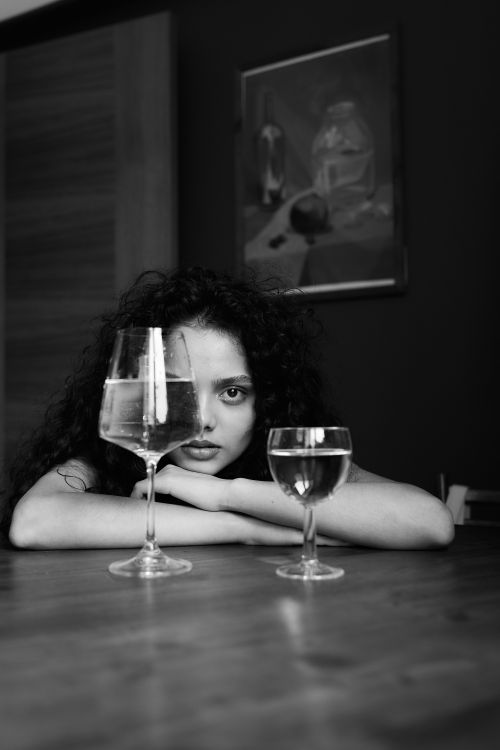 Free Intriguing monochrome portrait of a woman behind wine glasses, creating a surreal effect. Stock Photo