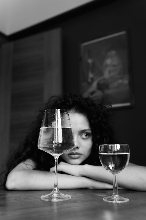Free Black and white portrait of a woman with wine glasses, conveying a moody atmosphere. Stock Photo
