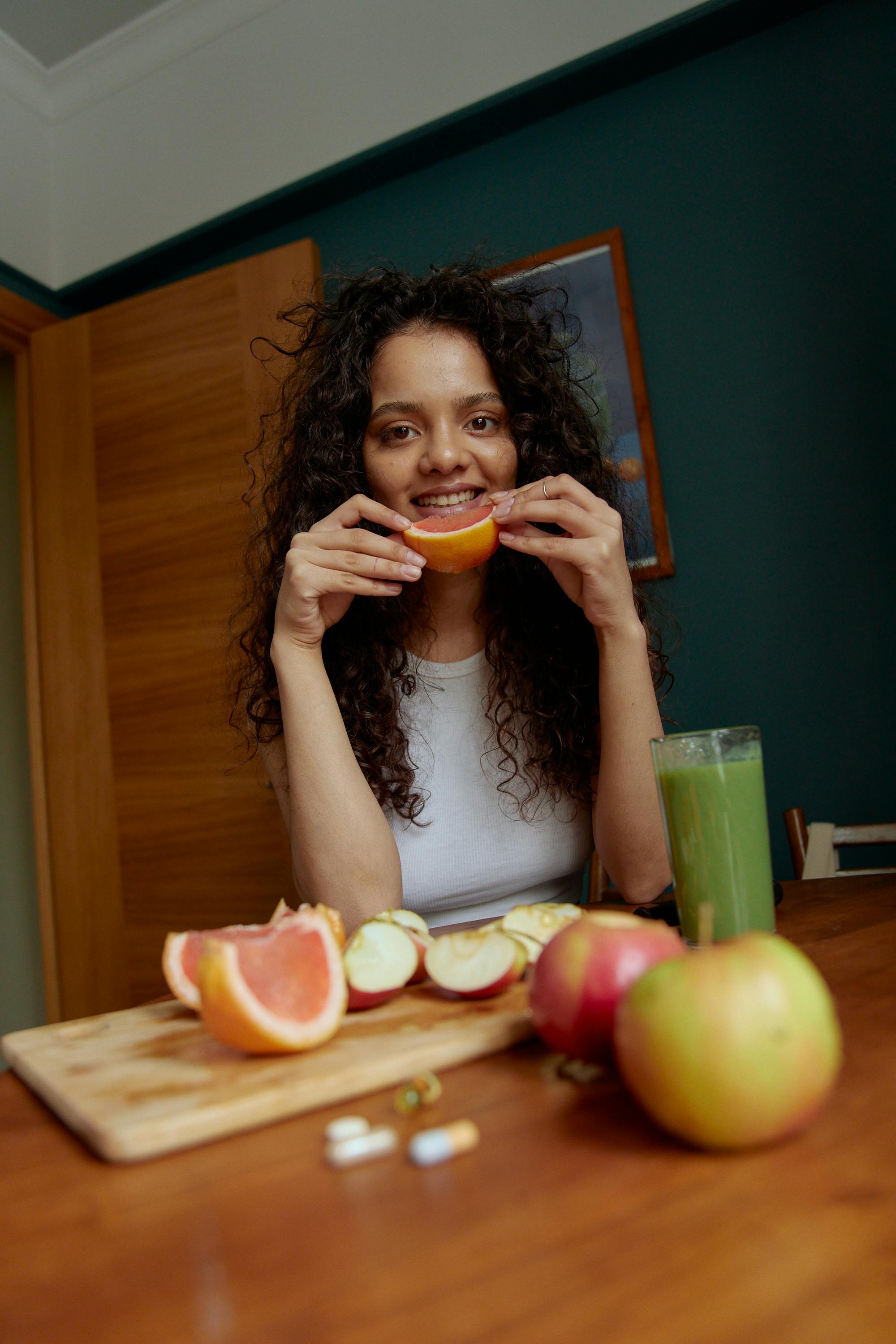 Young woman with curly hair enjoying a grapefruit and fresh juice at home, embracing a healthy lifestyle.