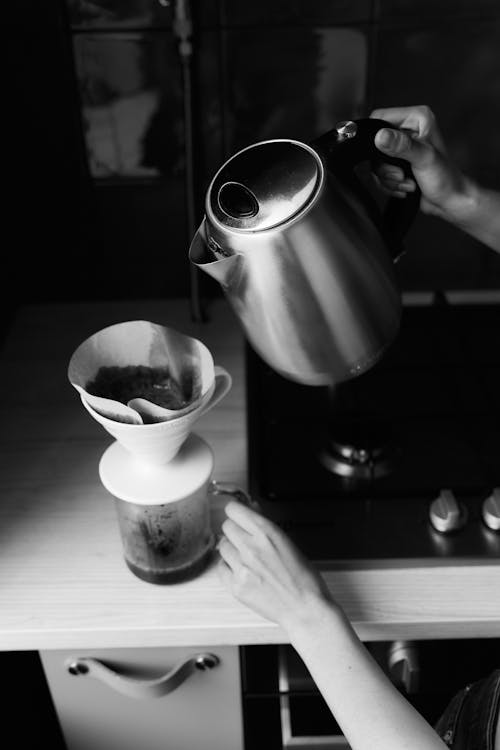 Grayscale Photo of Person Pouring Water on White Ceramic Teacup