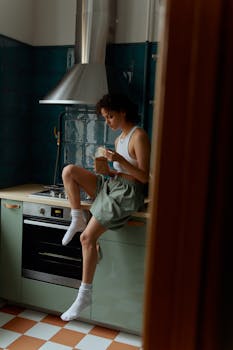 Young woman sitting on kitchen counter eating noodles, relaxed and casual atmosphere.
