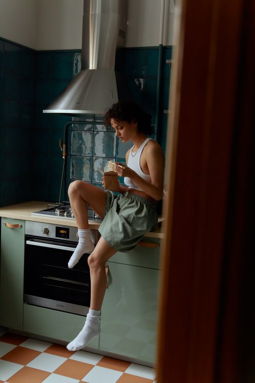 Free Young woman sitting on kitchen counter eating noodles, relaxed and casual atmosphere. Stock Photo