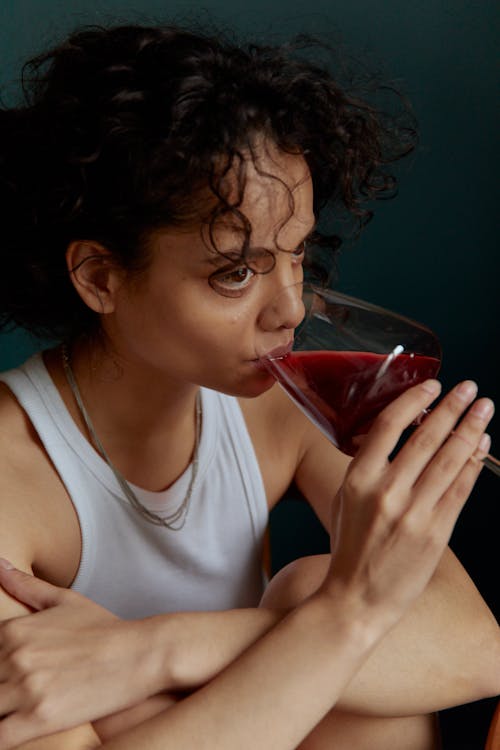 Woman in White Tank Top Drinking Red Liquid from Clear Drinking Glass