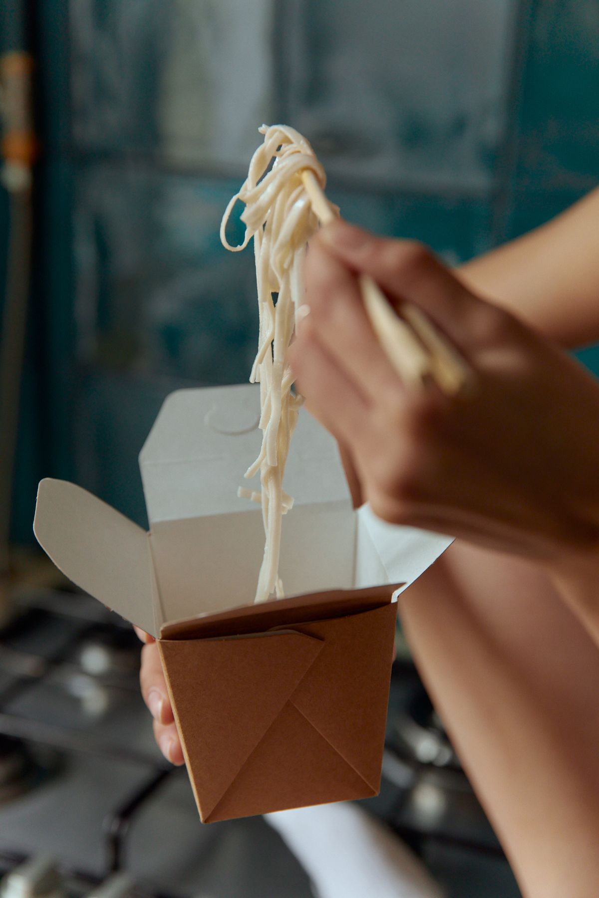 Noodles being lifted out of a takeaway box with chopsticks