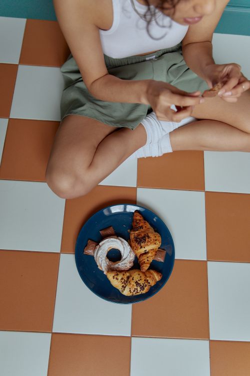 Free Woman sitting on tiled floor with croissants and donuts on a plate, high angle view. Stock Photo