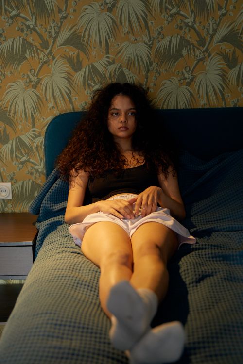 Free A young woman with curly hair lying on a bed in a cozy room, reflecting mood. Stock Photo