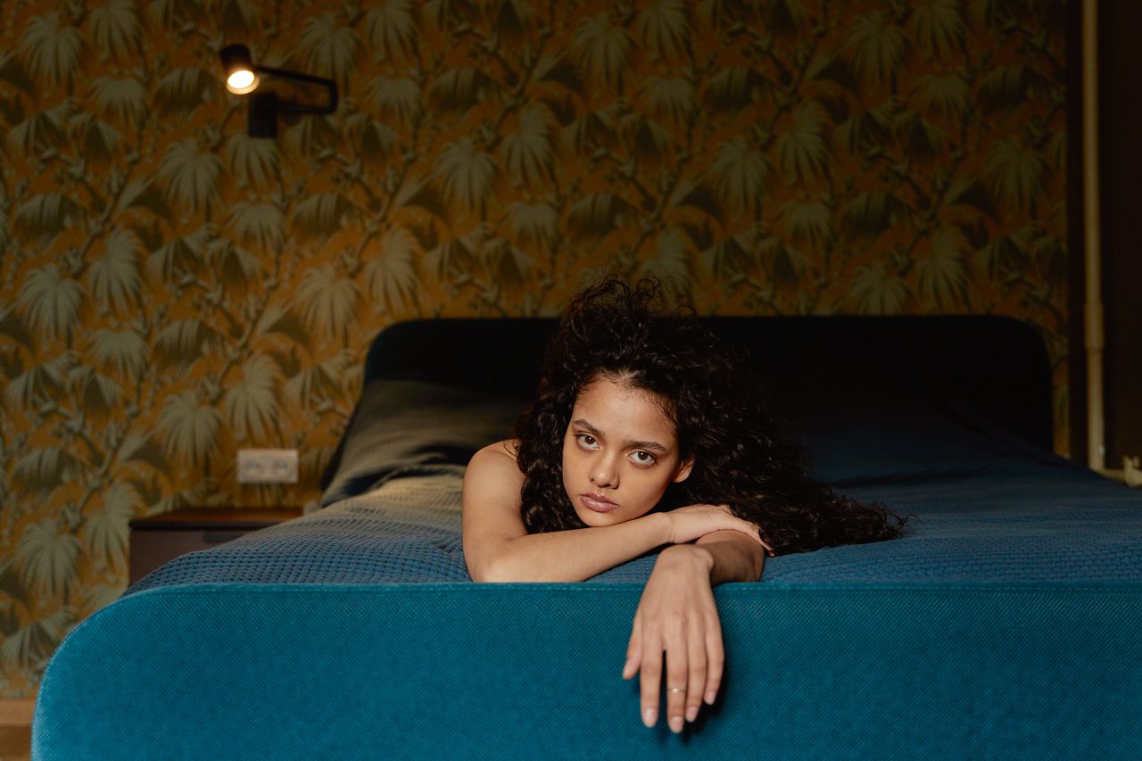 portrait of a young woman lying on a bed with a pensive expression ind