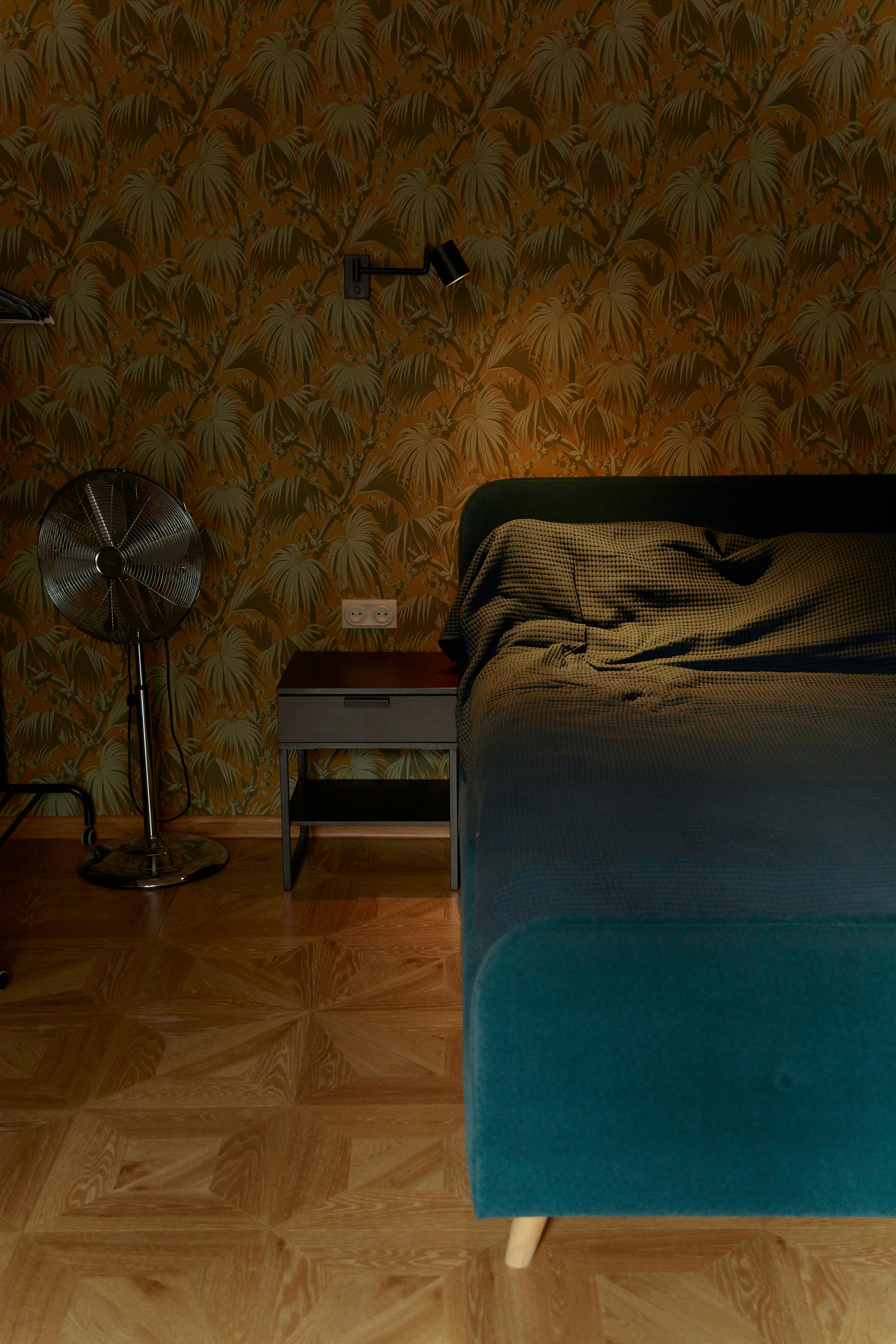 Stylish bedroom featuring a cozy bed, vintage wallpaper, and modern lighting.