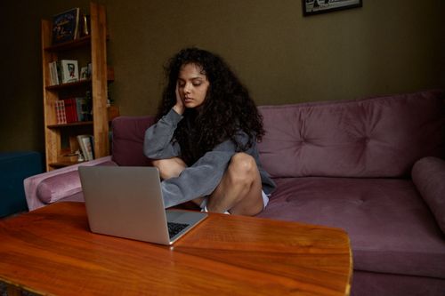 Free A young woman sitting on a sofa working on a laptop in a cozy home environment. Stock Photo