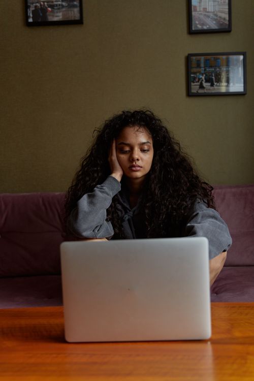 Free Woman with long curly hair sitting indoors, looking tired while working on a laptop. Stock Photo