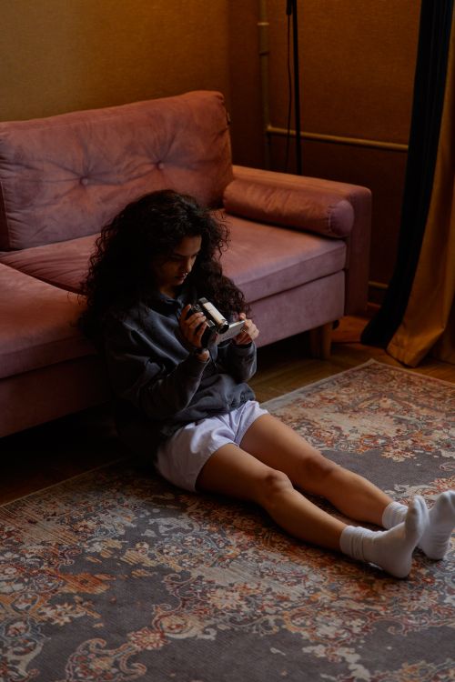 Free A young woman sits on the floor with a camera in a cozy indoor setting. Stock Photo