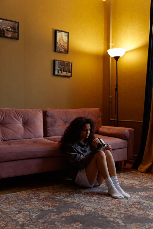 Free Woman sitting on the floor near a sofa, reflecting in a dimly lit living room. Stock Photo