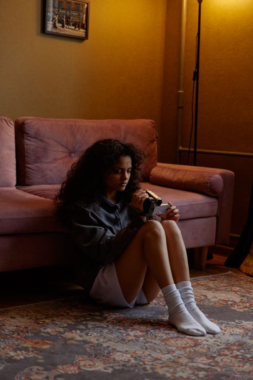 Free A young woman sitting on the floor holding a video camera indoors, with a cozy setting. Stock Photo