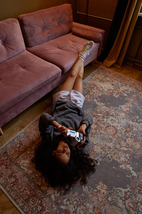 A Woman in Gray Sweater Lying on the Carpet while Holding a Video Camera