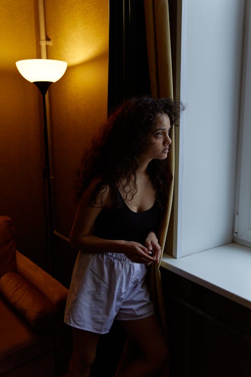 Free Woman in Black Tank Top Standing Beside a Curtain Stock Photo