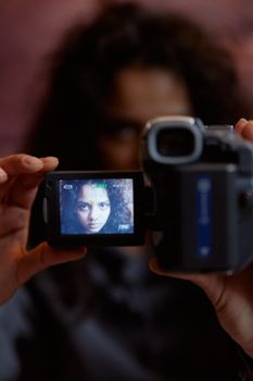 Woman holding a video camera with her face visible on the screen, indoors.