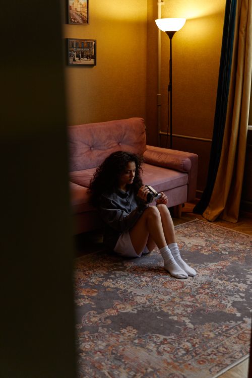 Free A young woman sitting on a rug in a cozy room holding a camera. Stock Photo