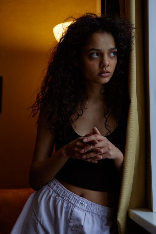 Free A thoughtful woman standing by a window, caught in a moment of introspection in a dimly lit room. Stock Photo