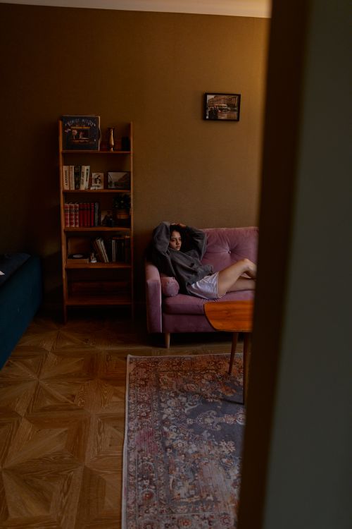 Free A woman in a gray sweater sitting on a pink sofa in a warm, cozy living room setting. Stock Photo