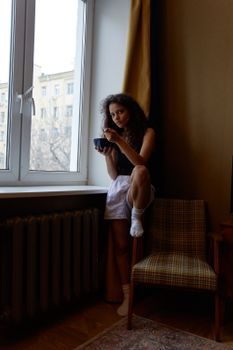 South Asian woman in a cozy room enjoys tea by the window, creating a serene and contemplative mood.