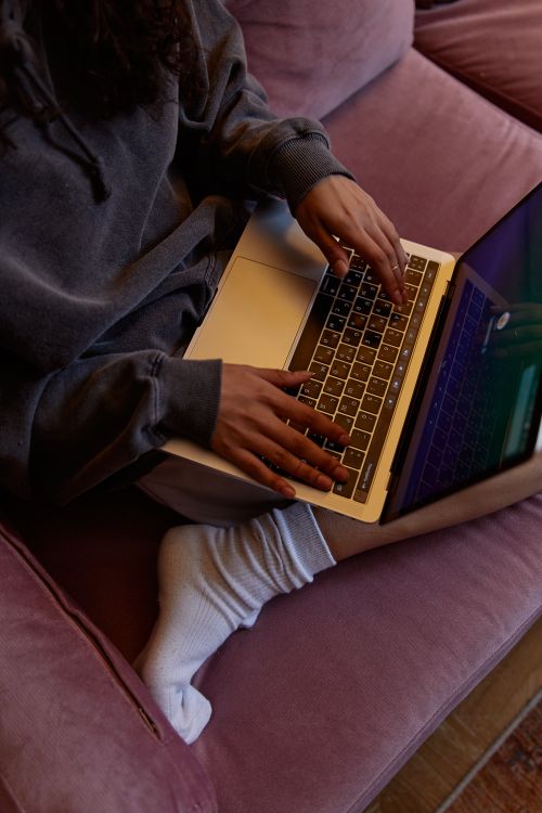 Free Person working remotely on a laptop from a cozy indoor sofa, showcasing technology and lifestyle. Stock Photo