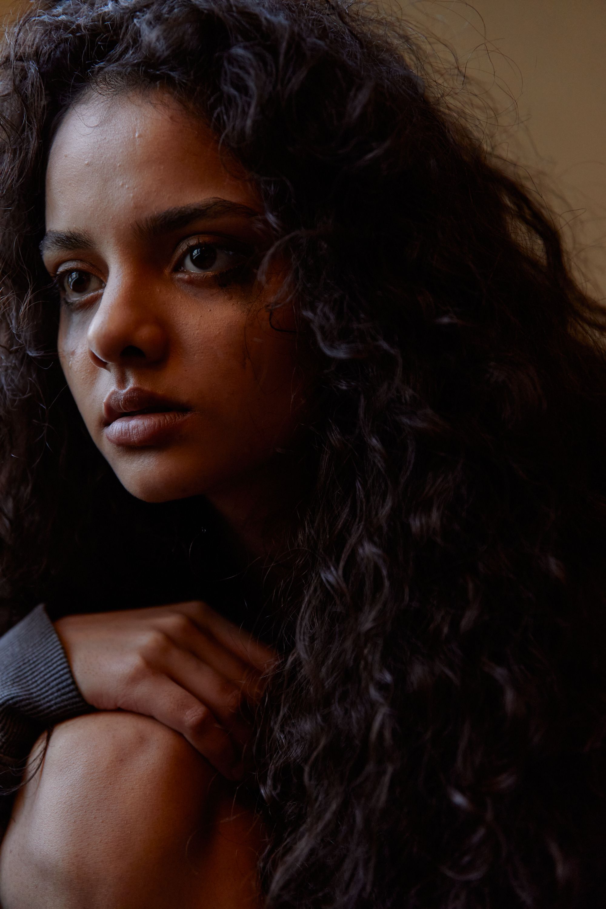 Close-up portrait of a young woman with curly hair, deep in thought.