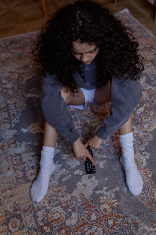 Woman in White Tank Top and Gray Cardigan Sitting on Brown and White Concrete Floor