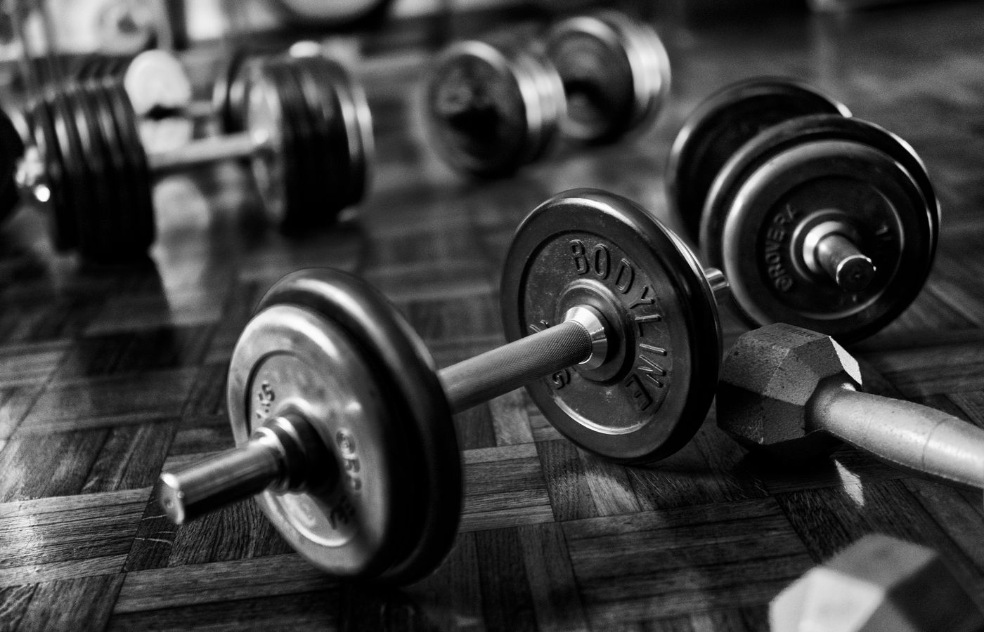 Black and white photo of gym dumbbells on a wooden floor, emphasizing strength and fitness.