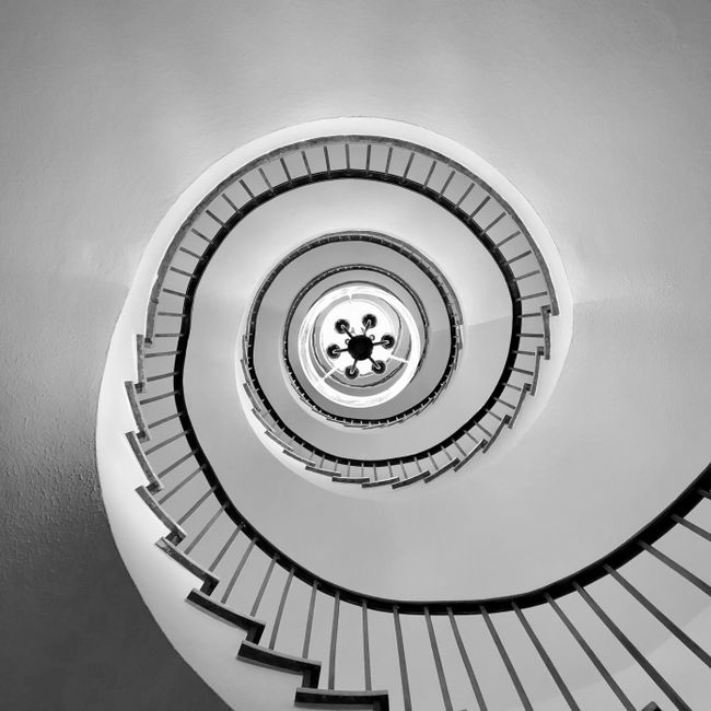 A striking black and white photo of an elegant spiral staircase with a chandelier.