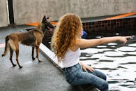 Side view of anonymous woman with curly hair pointing with finger at pool against attentive dog outdoors