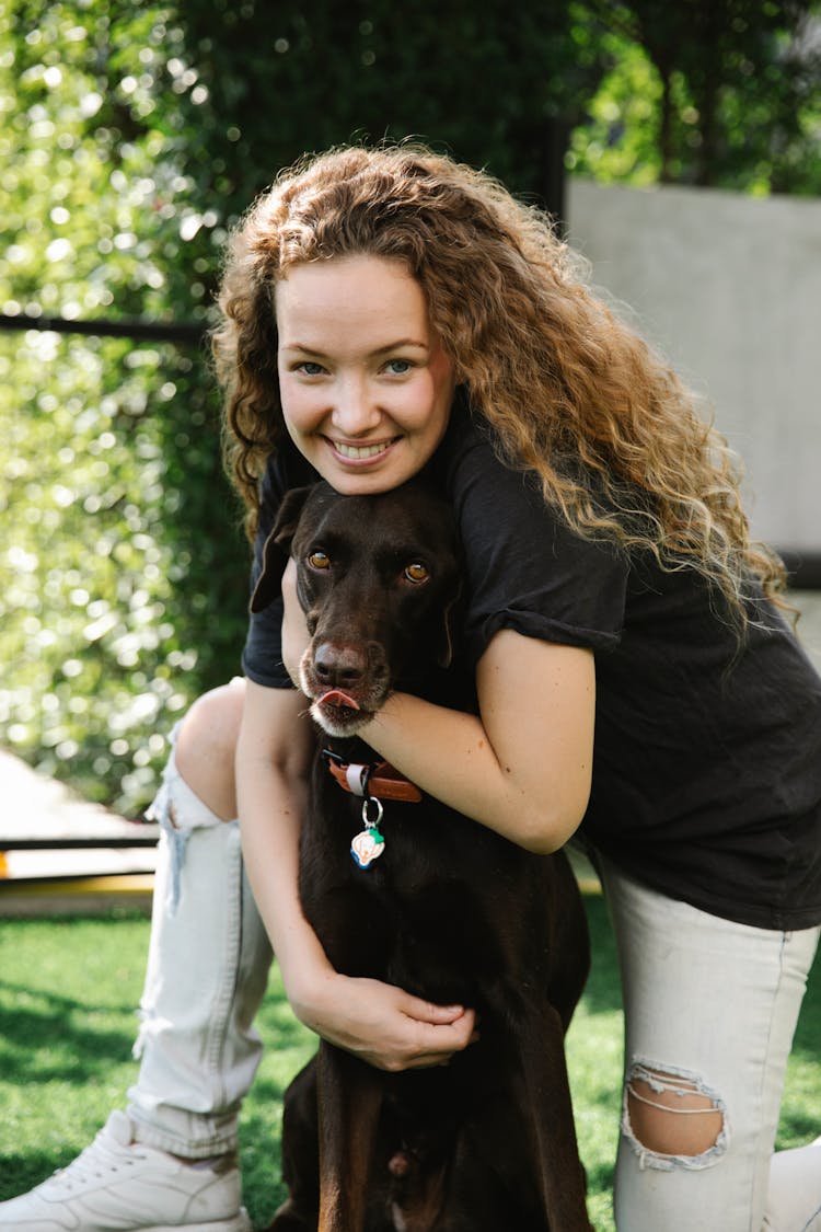 Cheerful Woman Embracing Bird Dog On Meadow