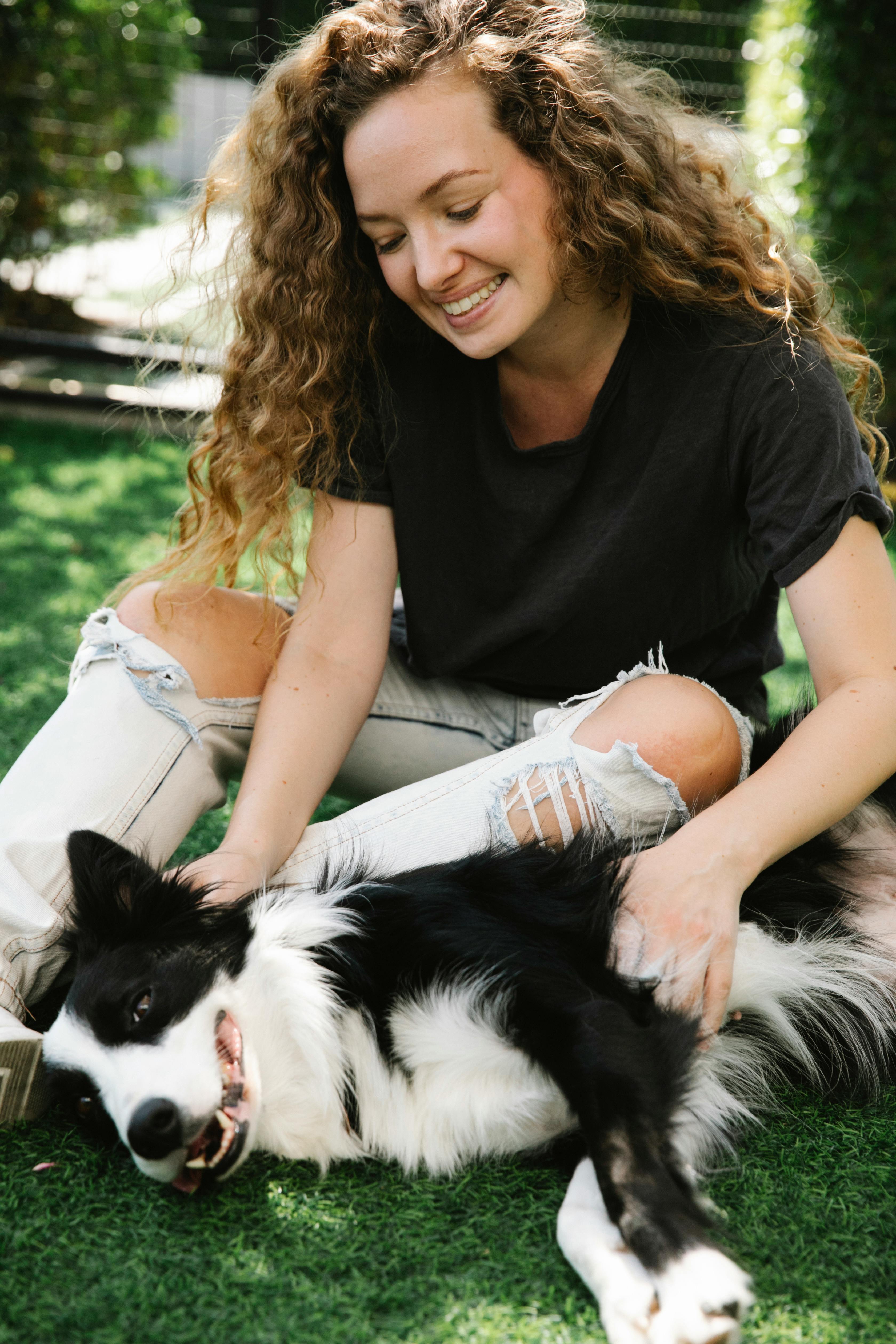 Smiling owner stroking Border Collie on lawn in summertime