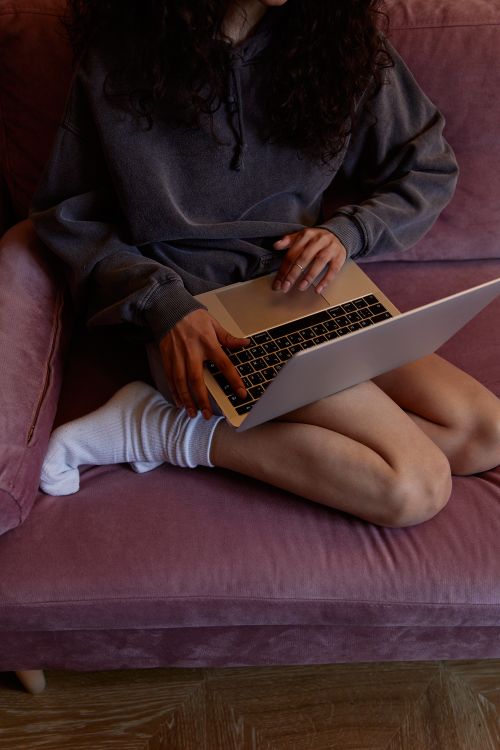 Free A young woman sits on a purple sofa using a laptop, showcasing a relaxed home environment. Stock Photo