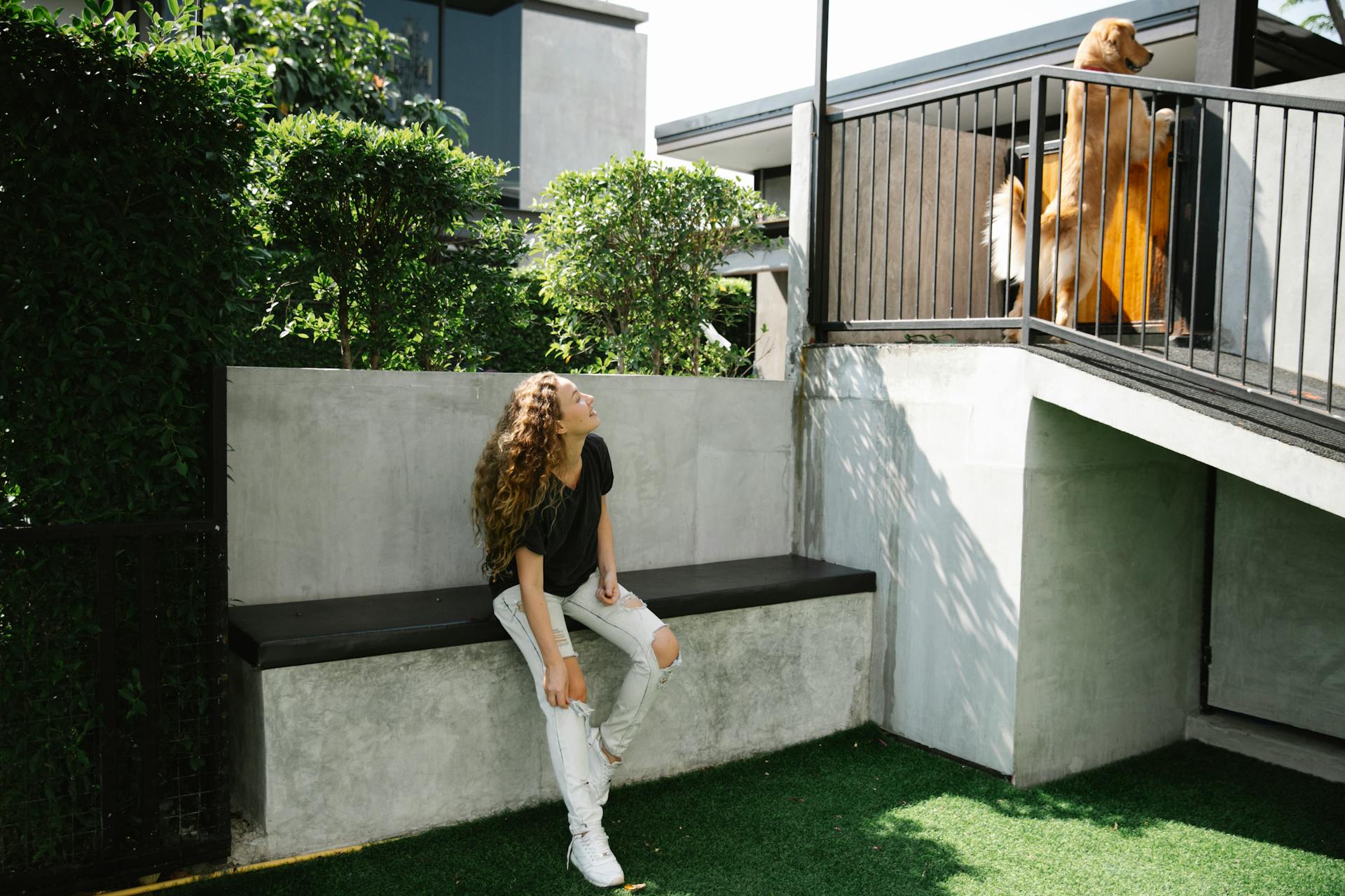 Glad female with long curly hair smiling and watching funny cute dog playing in yard